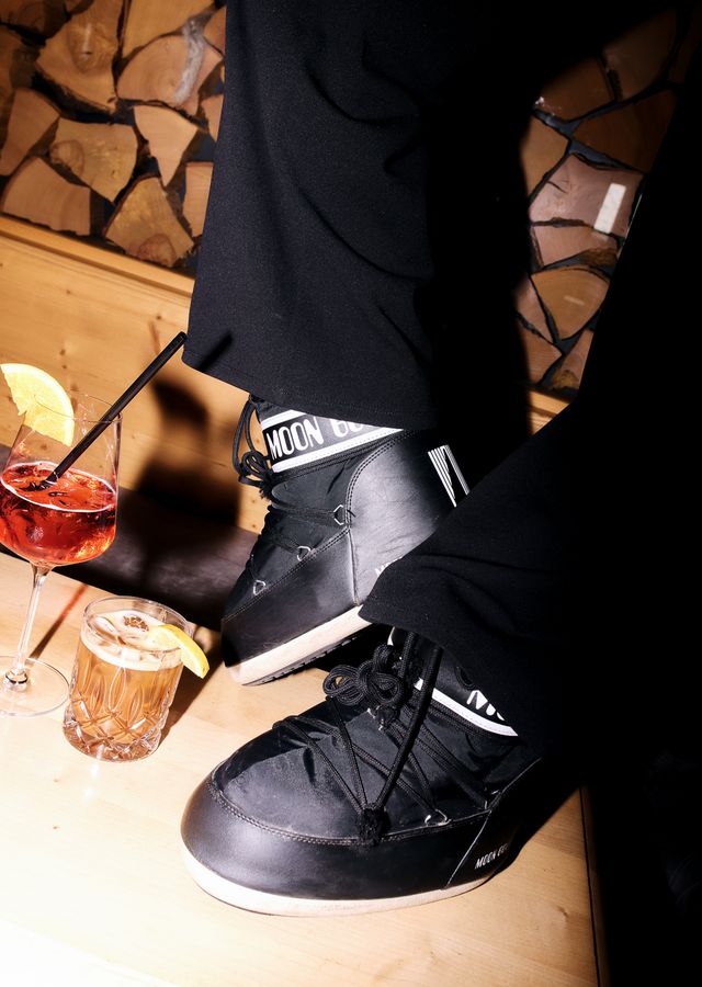 Ski boots and aperitif glasses on a wooden table by stacked firewood