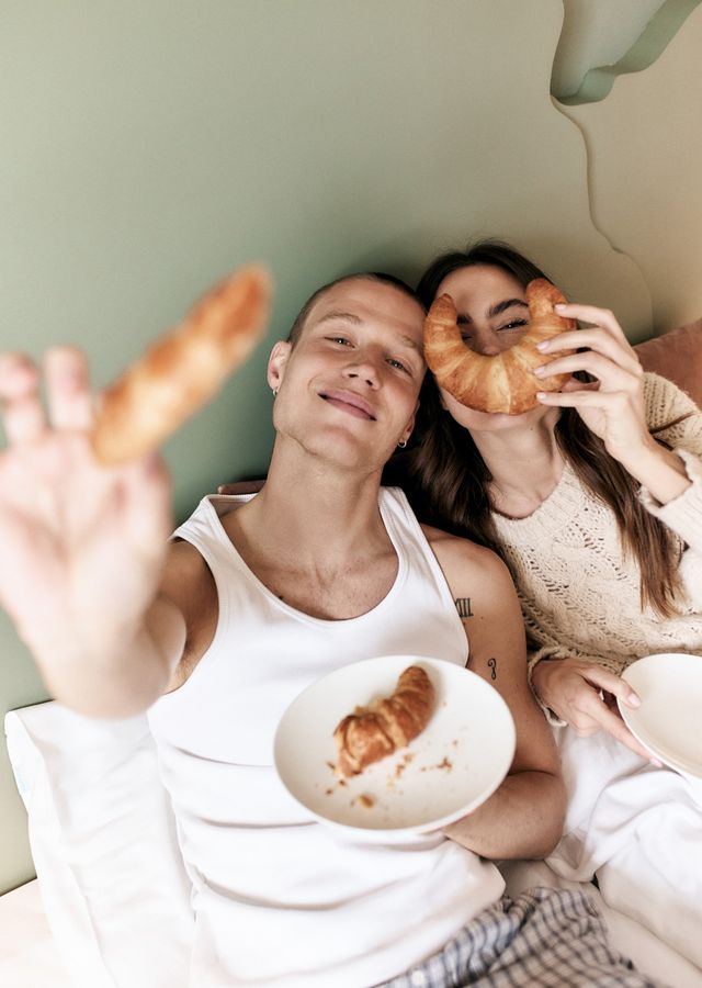 Couple in bed holding up croissants, laughing
