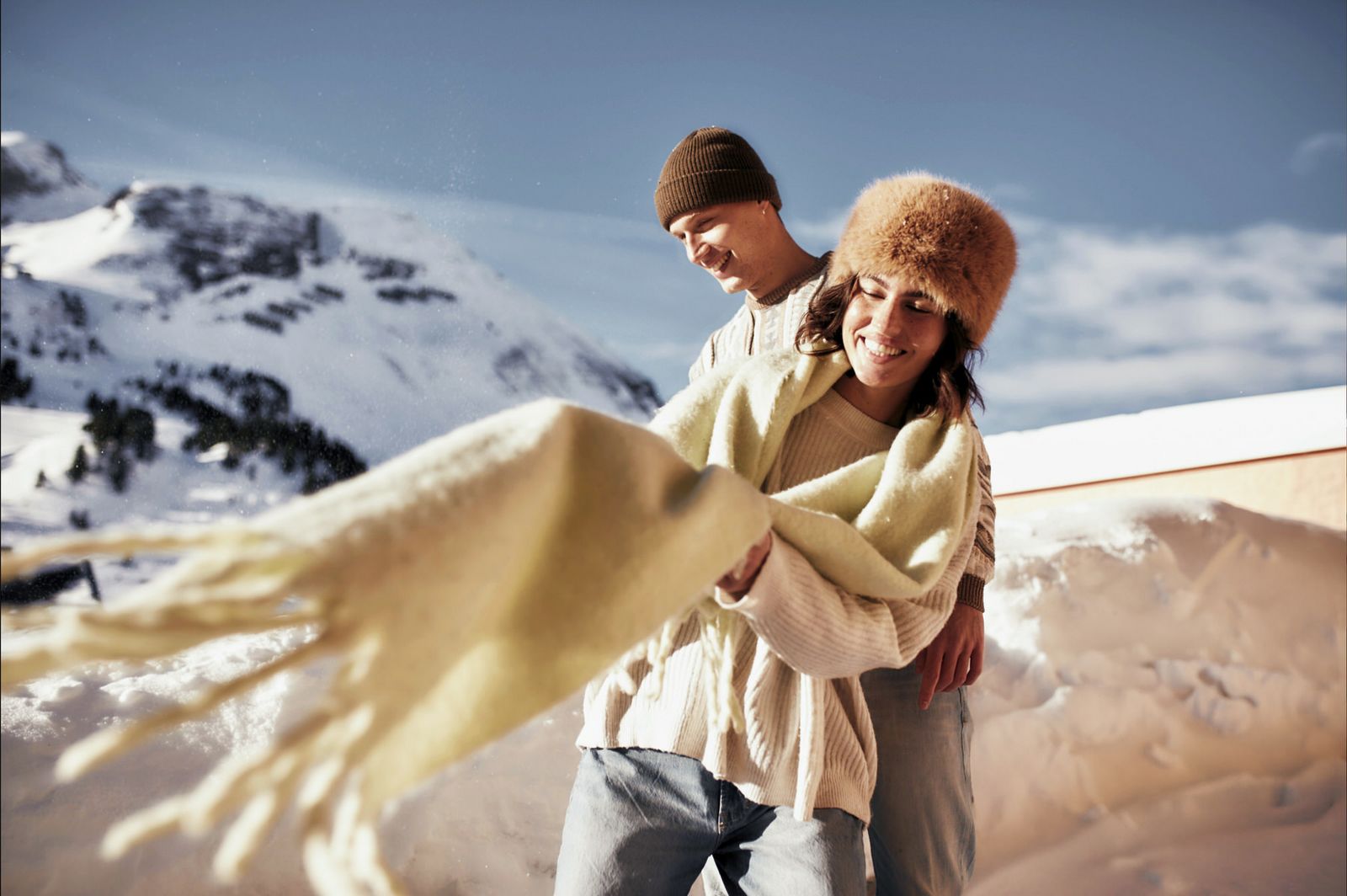 Laughing couple in winter clothing with a blanket in the snow